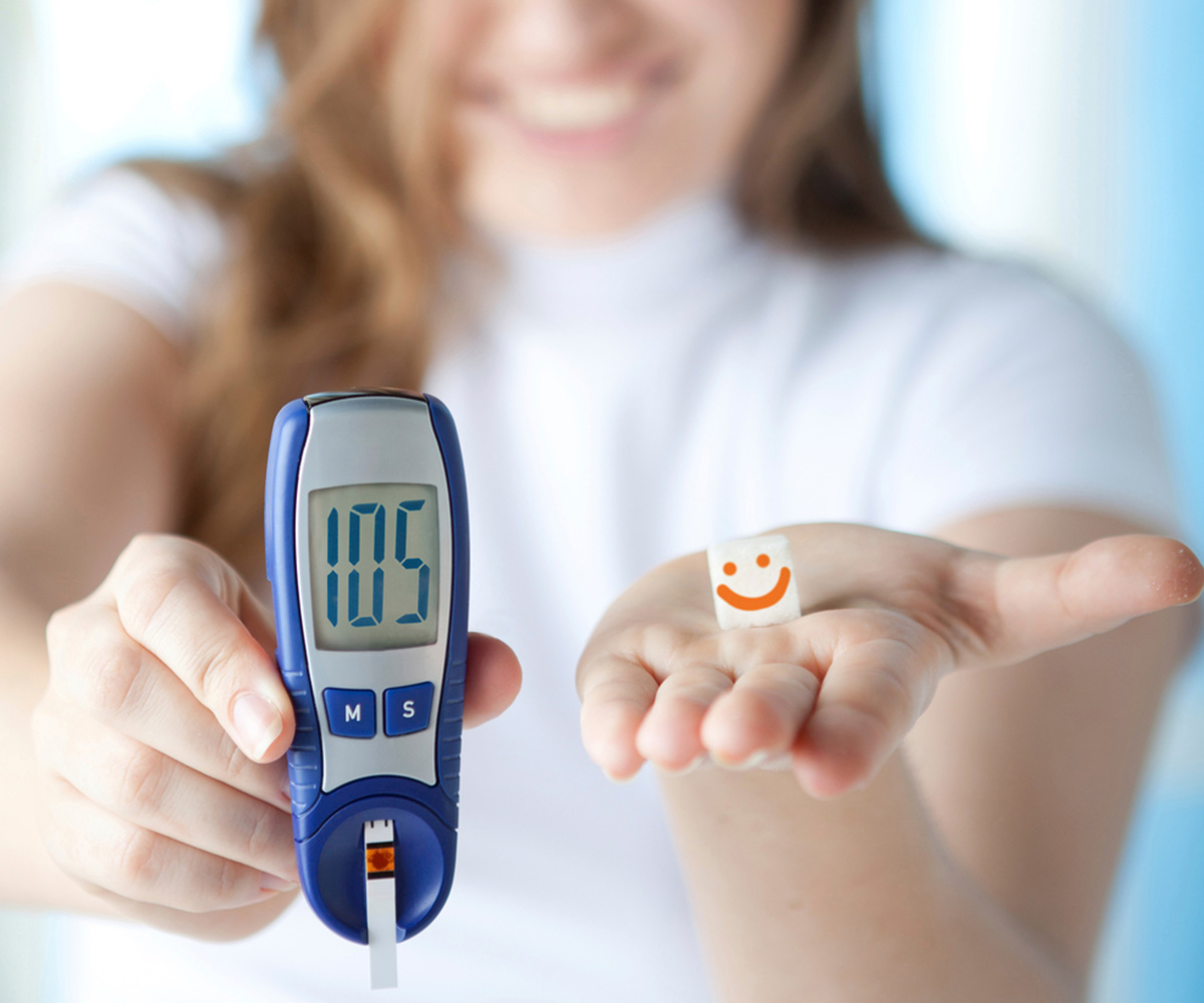 Woman holding a glucose monitor in one hand that reads 105 and a smiley face in the other hand, she is smiling in the background indicating well managed blood glucose levels after diabetes treatment with Stamford Physical Medicine.